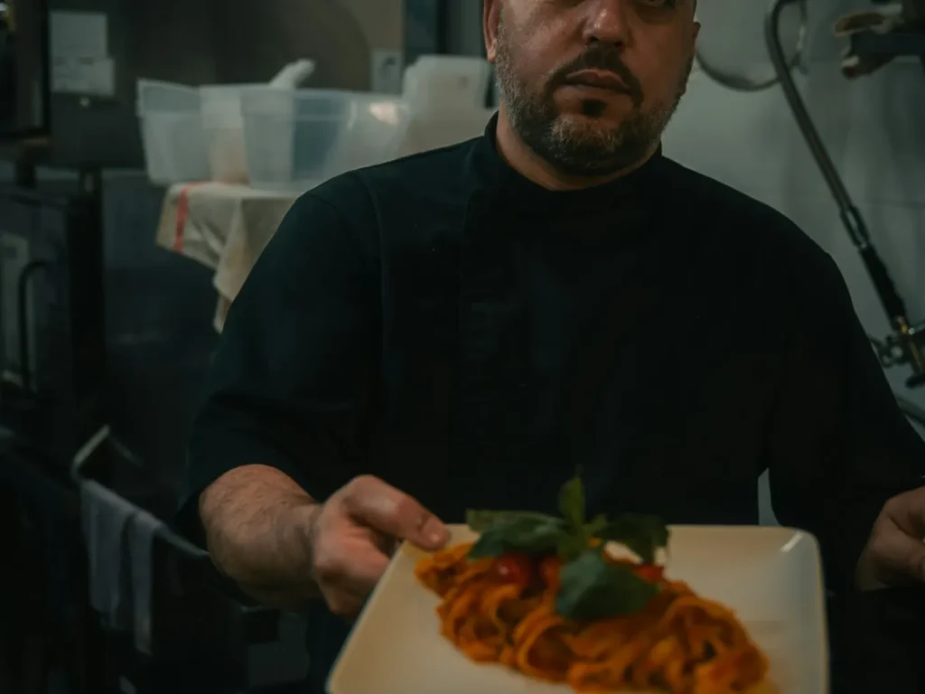 Chef de farda preta segura prato de massa na cozinha, fotografia de gastronomia para restaurantes