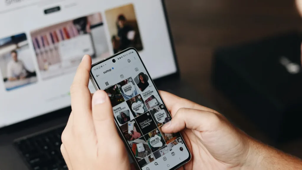 Pessoa a usar o telemóvel em frente ao portátil para gerir as redes sociais de uma empresa