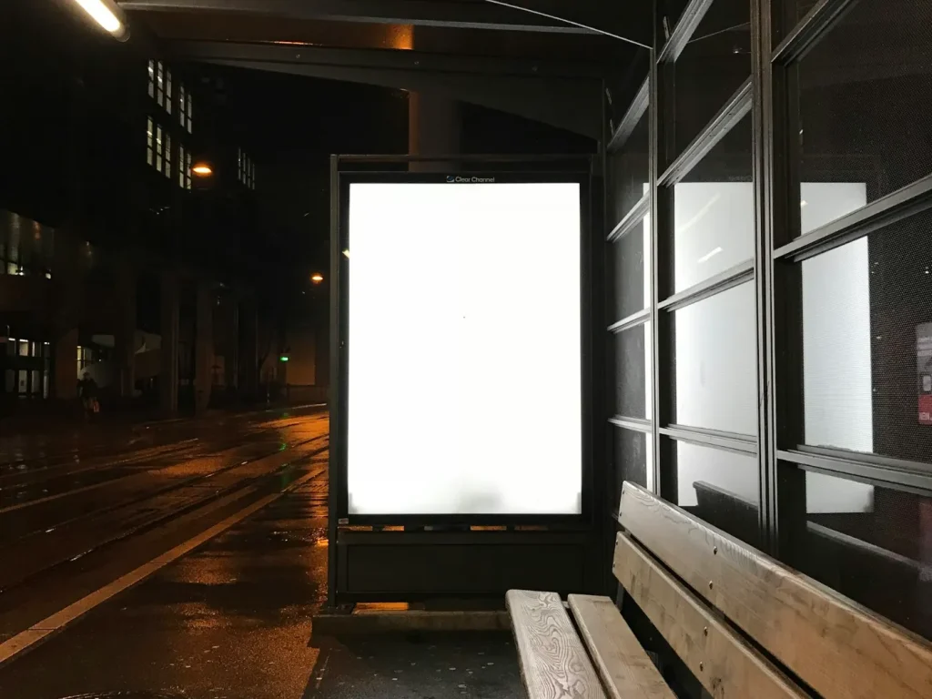 Mupi publicitário iluminado numa paragem de autocarro à noite, publicidade em outdoors e mupis