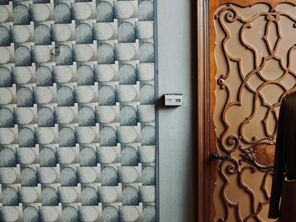 Parede revestida com papel de parede padronizado junto a porta de madeira trabalhada, papel de parede personalizado