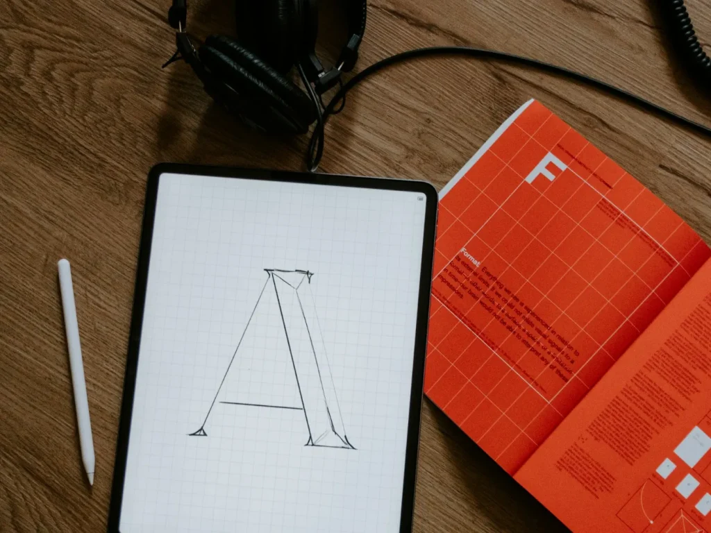 Tablet com esboço de letra, caneta digital e livro sobre madeira, rebranding de marcas