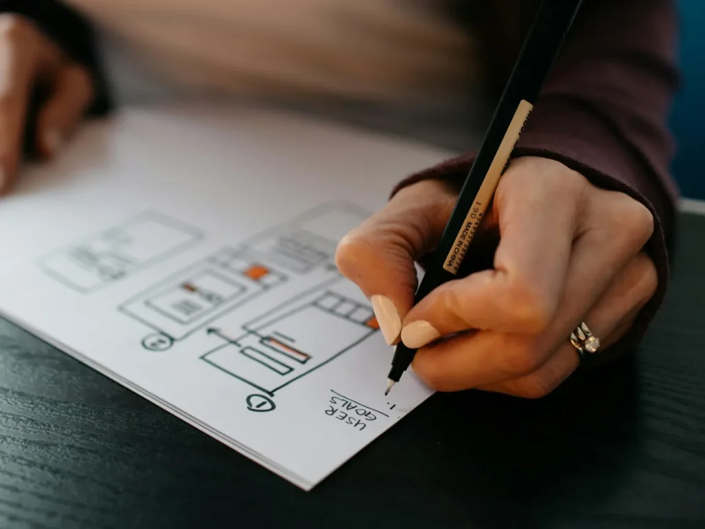 Mão a desenhar novo esboço de interface em papel, renovação de sites para empresas