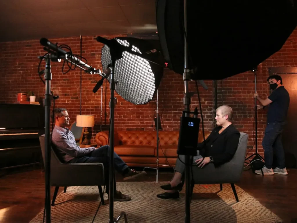 Duas pessoas sentadas diante de câmara de vídeo em entrevista, produção de vídeo institucional
