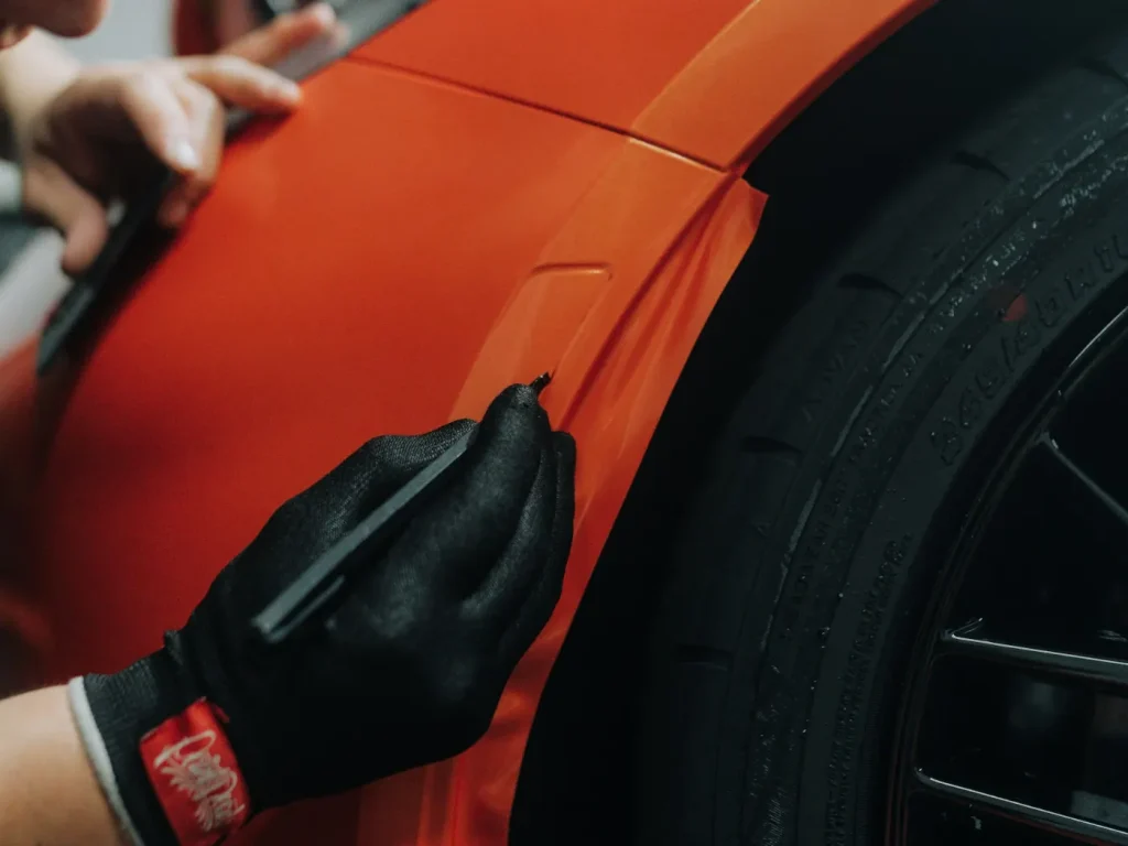 Técnico a aplicar película de vinil laranja num automóvel, wrapping de carros em Bragança
